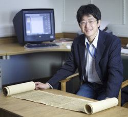 Kazushi Iwao standing at a table with a scroll unrolled in front of him.