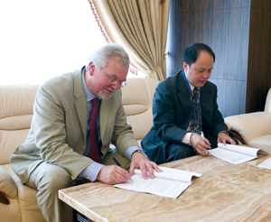 Two formally dressed men, seated, signing documents.