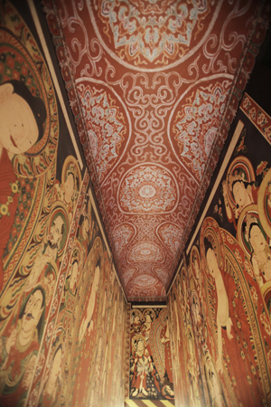 Interior photograph looking upwards in a space with brightly illustrated wall paintings and a red decorated ceiling.