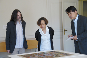 Three scholars looking at a painting on a flat surface.