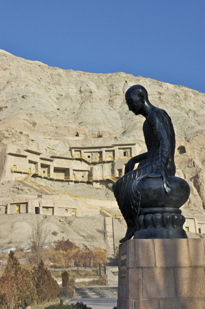 Black statue silhouetted against a cliff face with built-up caves. 