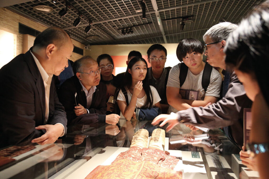 A group of people looking at a glass case containing textile materials.