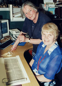 Two people at a desk where a scroll has been unrolled.