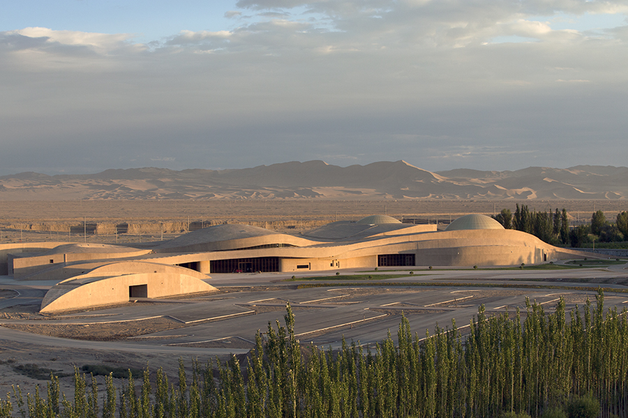 Photograph of a modern building in the desert, built in a shape evocative of sand dunes. 