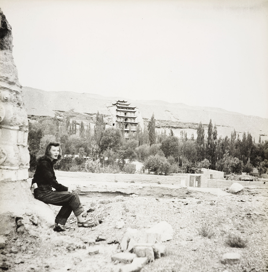 Irene Vincent sitting against a stele outside the Dunhuang Mogao Caves, historical black and white photograph.