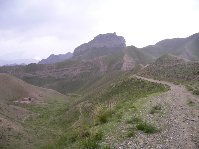 Modern landscape photograph of a path in mountainous terrain, with low lying vegetation.