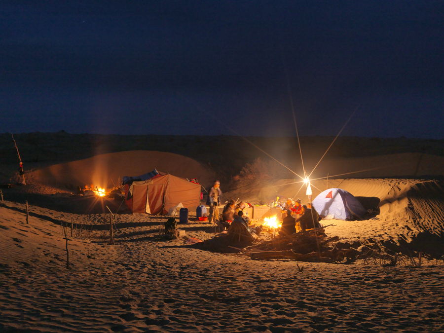 Night time photograph of a camp with tents set up and people sitting around a fire.