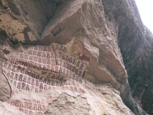 A cliff face under a rocky outcrop which has been painted with a repeated pattern in red.