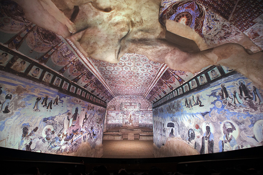An indoor space where light projection is used to show what a fully decorated Mogao cave would have looked like, with brightly coloured walls and ceiling.