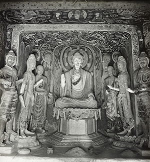 Elaborately carved cave temple interior with statues of a Buddha and bodhisattvas.