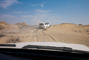 A vehicle driving through the sand, creating a cloud of sand as it turns. 