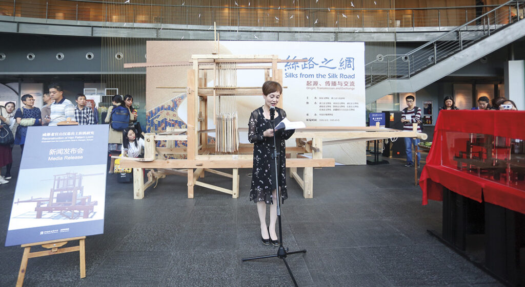 A person standing at a microphone, giving a talk in a museum space. 