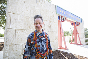 Headshot of Peter Sellars, smiling by a sign that reads Cave Temples of Dunhuang.