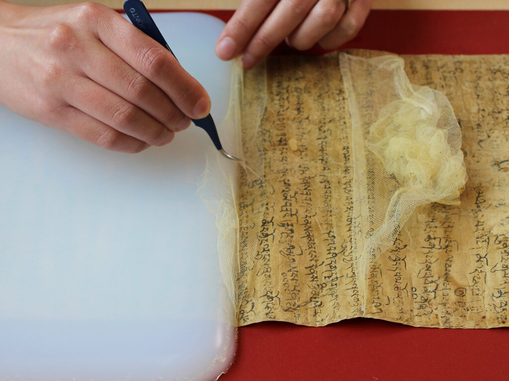 A conservator using a tool to remove gauze from a manuscript.