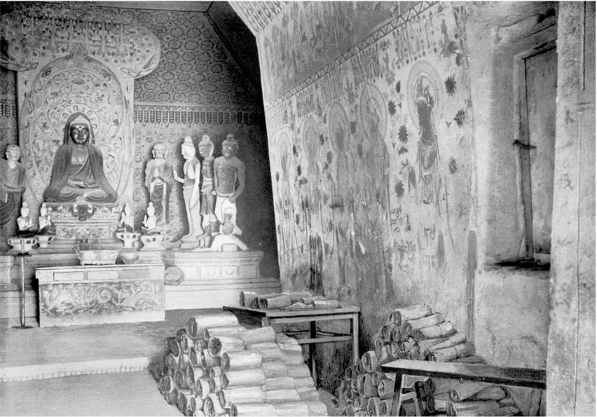 Cave interior with statues and murals, and scroll bundles in piles on the floor. The entrance to Cave 17 looks like a hatch, above waist height. 