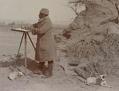 A cartographer in the desert, with a dog. Historic black and white photograph.