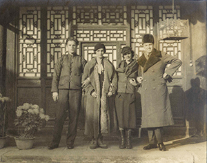 Four people in coats standing in front of a house with elaborate latticework on and around the front door. Historical sepia photograph.
