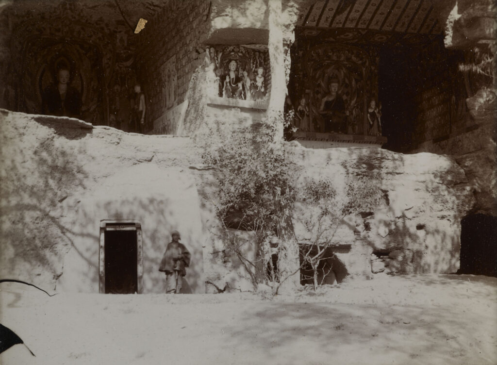 Two cave grottoes open to the air, with wall paintings and statues visible. Historic black and white photograph. 