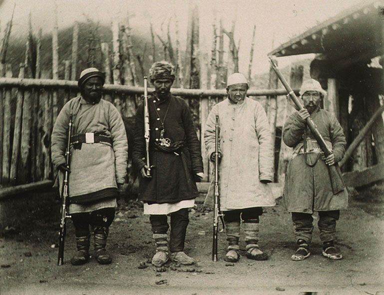 Four men in cold weather clothes with weapons. Historic black and white photograph. 