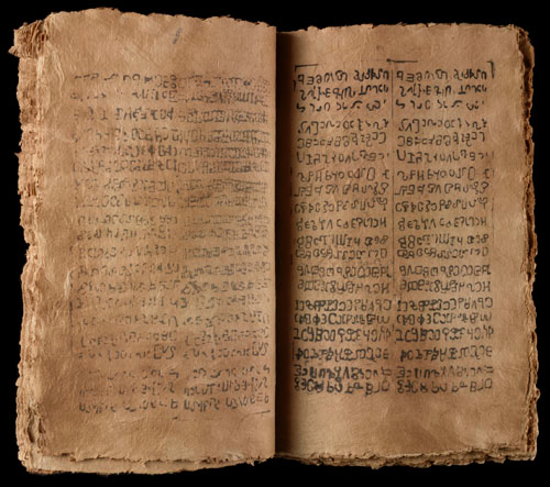 A codex form printed book in a made up language, on brown rough-edged paper.